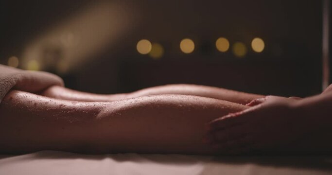 Hands of professional massagist rubbing pink scrub in female legs during massage procedures. Organic cosmetics used in healthy skin care wellness relaxation therapy 4k footage