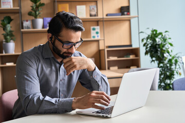 Latin indian serious businessman wearing glasses and headset having virtual team meeting call,...