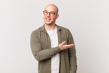 bald man smiling cheerfully, feeling happy and showing a concept in copy space with palm of hand