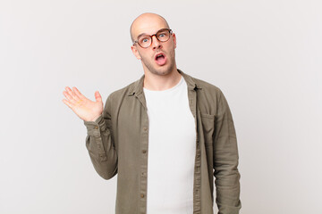 bald man looking surprised and shocked, with jaw dropped holding an object with an open hand on the...