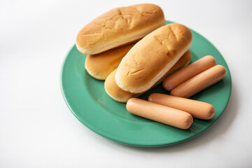 Fresh hot dog buns which lie on a green plate along with sausages. Top view, close-up.