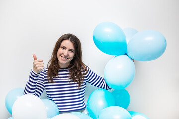 Fototapeta premium Happy girl in a striped sweater smiles and holds blue balloons in her hands. Place for an inscription, holiday concept.