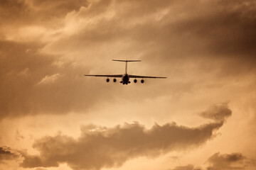 Ilyushin aircraft seen from behind during take off at low altitude in a vintage photo effect. Russian four-engine airplane silhouette in a gold color. Russian plane constructor.