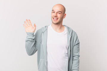 bald man smiling happily and cheerfully, waving hand, welcoming and greeting you, or saying goodbye