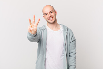 bald man smiling and looking friendly, showing number three or third with hand forward, counting...