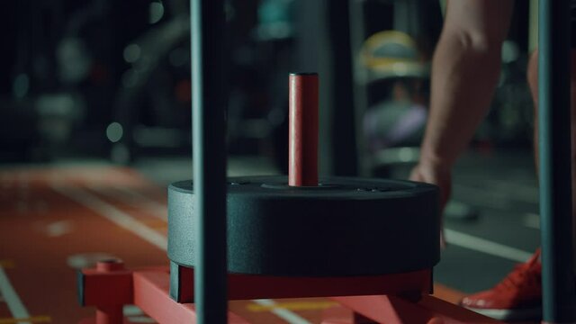 Barbell plates are put on stand for exercising by muscular man in dark gym. Closeup bodybuilder preparing equipment for workout. Concept of sport