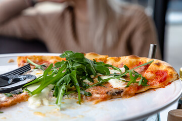 Pizza with arugula and burata is on a plate in a restaurant.