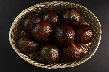 Ripe avocados in a basket on a black table, with a cut fruit and a stone.