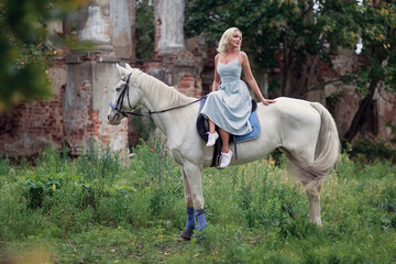A beautiful woman in a blue dress rides a white horse. Best friends. Photoshoot with a horse. Hobby...