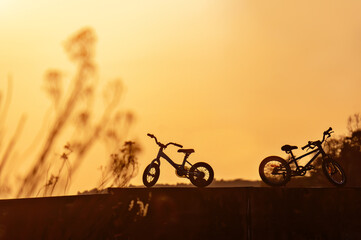 Two silhouettes of children's bicycles on the background of a warm sunset.