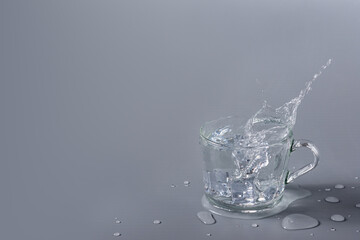 Crystal clear water with ice in transparent glass cup on a gray background. Splash and splash