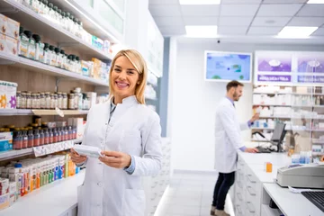 Photo sur Plexiglas Pharmacie Portrait d& 39 une belle pharmacienne debout dans une pharmacie près de l& 39 étagère avec des médicaments.