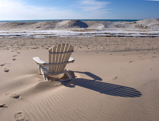 Chair on sandy beach on shoreline casting a shadow