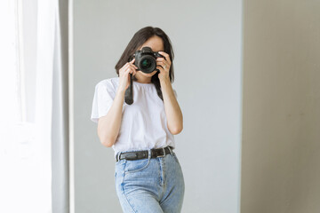 a young woman with black hair and a white T-shirt takes a picture of herself on a SLR camera through the mirror. the girl is engaged in hobbies, takes pictures, shoots her blog