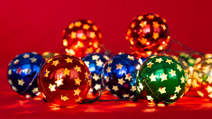 Decorative Christmas glowing garland lights multi-colored balls with star shaped holes. Red, green, yellow and blue balls on a red background, festive horizontal photo 
