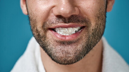 Obraz premium Close up of bearded man smiling at camera with toothpaste in his mouth after brushing teeth isolated over blue background