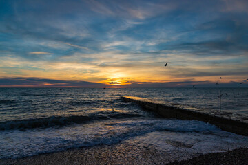Beautiful sunset over the sea and stone pier with clouds and horizon on the beach in Sochi, Russia