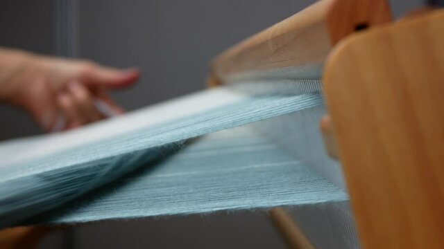 Process of weaving side view, close up. Shuttle is carrying the crosswise threads through the lengthwise threads. Loom details