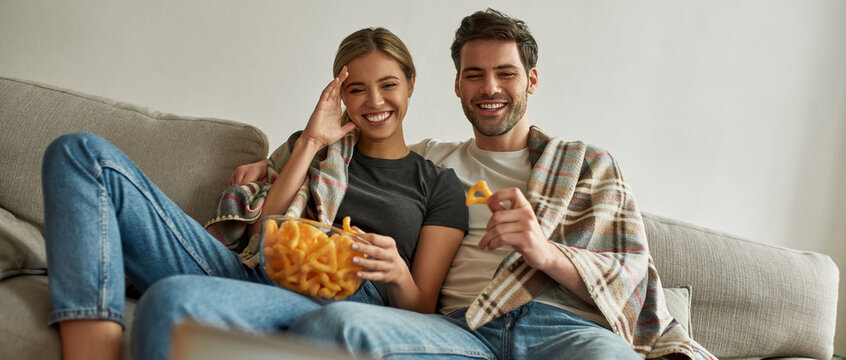 Picture of a young couple watching comedy at home under plaid