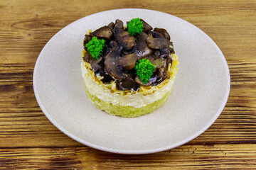 Tasty layered salad with roasted mushrooms, potato, eggs, cheese and mayonnaise on wooden table