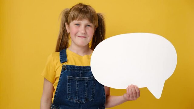 Cute little girl kid holding an empty white speech bubble, ponders on decision, thinking about something, holds hand on chin, isolated over yellow background with copy space. Hmm something strange