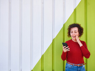 Woman using her mobile phone looking surprised with a green and white wall in the background