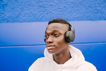 Young afro American black man listening music with wireless headphones while wearing a white sweatshirt, looking to the side