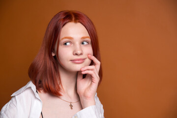 Red-haired girl on a brown monochrome background. Large portrait. A surprised look to the side.