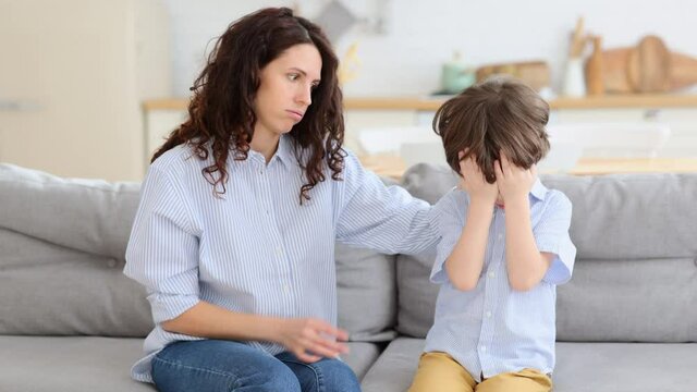 Caring mom supporting little preschool son. Beautiful female parent comfort crying offended kid. Small boy upset, stressed, abused or frightened with nervous supportive mother on couch in living room