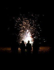 People in Silhouette Watch Fireworks Explode on Beach in Pitch Dark - 429099861