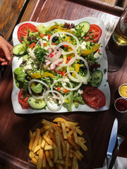 Großer Teller mit gesundem Salat, Oliven, Radieschen, Tomaten, Peperoni, Schafskäse, Gurke, Zwiebeln und Pommes Frites