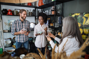 Happy Caucasian man and african woman listening to gray-haired saleswoman while choosing exclusive ceramic goods at decor store. Couple buying goods at shop. Shopping concept.