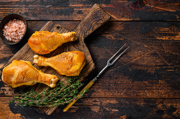 Marinated and Smoked chicken legs drumsticks on a wooden cutting board. Dark wooden background. Top view. Copy space