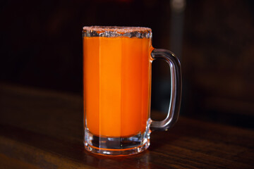 Michelada beer with tomato juice. Clamato with beer on wooden table. Mexican drink. Michelada beer with tomato juice, shrimps, clam and lemon, mexican drink cocktail in mexico. Concept of mexican beer