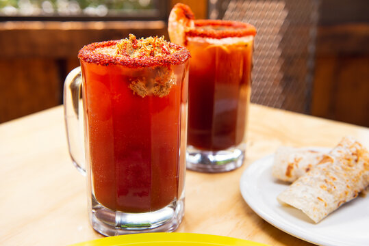 Michelada beer with tomato juice. Clamato with beer on wooden table. Mexican drink. Michelada beer with tomato juice, shrimps, clam and lemon, mexican drink cocktail in mexico. Concept of mexican beer