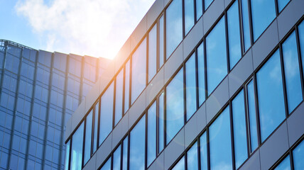 Blue sky reflection in glass facade of building. View of office building windows close up with sunrise, reflection and perspective.. Glass facade on a bright sunny day with sunbeams on the blue sky. 