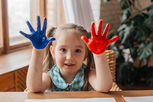 Portrait of a cute little girl draws with paints and hands. Painted children's palms. Close up. 