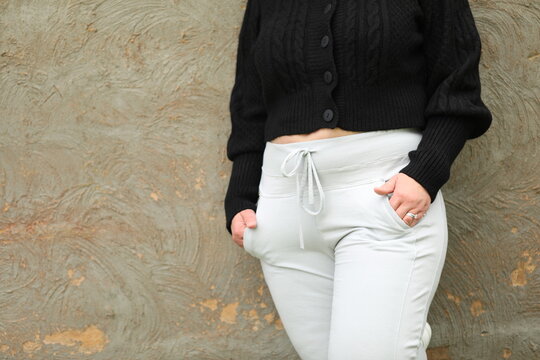 Fashion image of plus size woman wearing black wool top and light trainer pants leaning against concrete wall with copy space