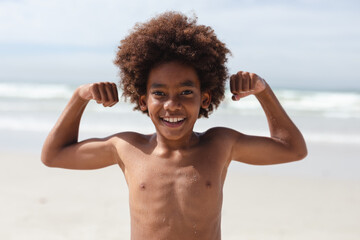 Portrait of african american boy flexing his biceps at the beach