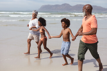 African american grandparents and grandchildren holding hands walking on the beach