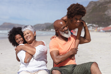 African american grandparents and grandchildren hugging while siting on the beach