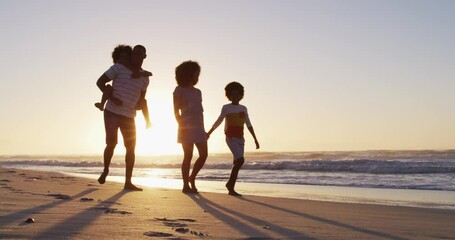 African american family having fun walking together during sunset on the beach - Powered by Adobe
