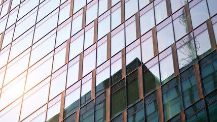 Fototapeta na wymiar Blue sky reflection in glass facade of building. View of office building windows close up with sunrise, reflection and perspective.. Glass facade on a bright sunny day with sunbeams on the blue sky. 