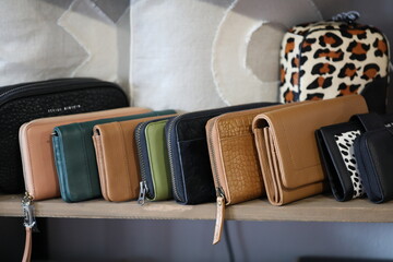 Row of brown, beige and black women's leather wallets on shelf in fashion boutique