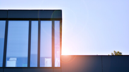 Blue sky reflection in glass facade of building. View of office building windows close up with sunrise, reflection and perspective.. Glass facade on a bright sunny day with sunbeams on the blue sky. 