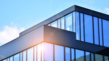 Fototapeta premium Blue sky reflection in glass facade of building. View of office building windows close up with sunrise, reflection and perspective.. Glass facade on a bright sunny day with sunbeams on the blue sky. 