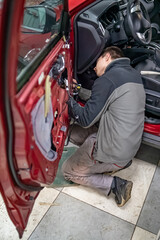 Mechanic guy in automobile service stay on a knees near car door at time of it dismantling to repair car after road accident