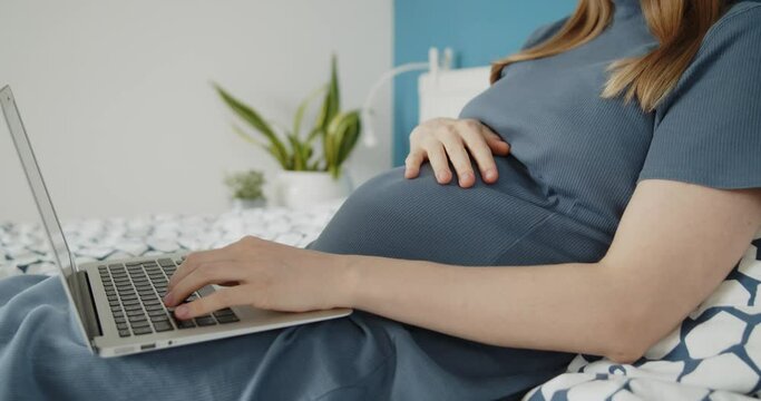 Young pregnant woman work on a laptop lying down on a bed in domestic environment. Concept of remote work, remote education, work during pregnancy and freelance.