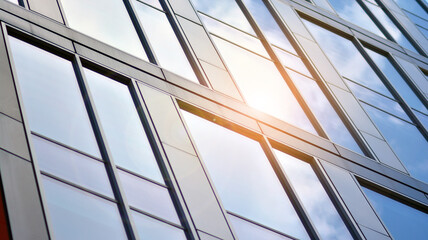 Blue sky reflection in glass facade of building. View of office building windows close up with sunrise, reflection and perspective.. Glass facade on a bright sunny day with sunbeams on the blue sky. 