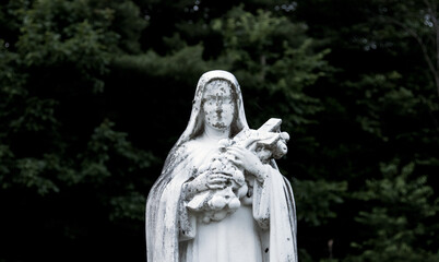 Statue of the Virgin Mary outside in a church cemetery with a dark green nature background